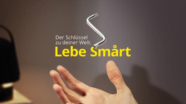Hand wirft einen IKEA-Inbusschlüssel in die Luft vor grauem Hintergrund mit dem Text „Der Schlüssel zu deiner Welt Lebe Smårt“ in Weiß und Gelb