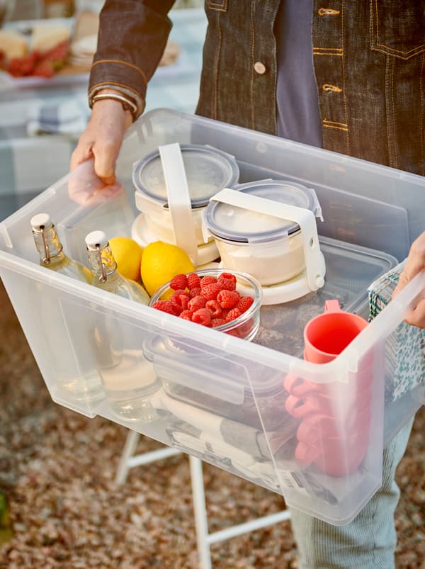Hands holding a SAMLA box full of tableware, glass bottles and food containers attached to IKEA 365+ ice packs.