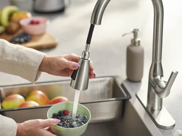 Hands rinsing berries in a bowl under a kitchen faucet.