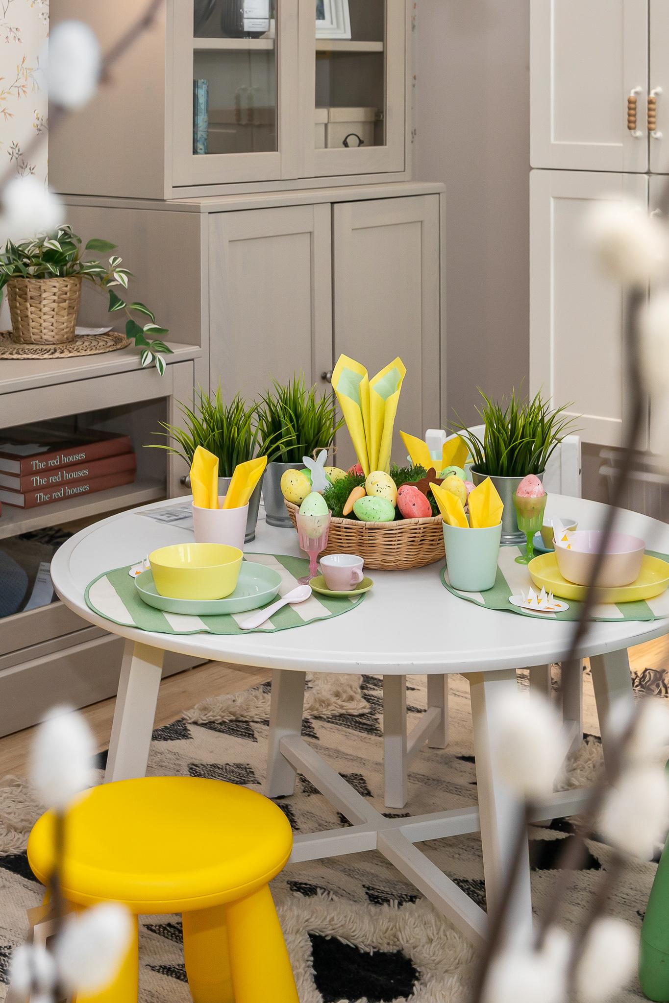 Hanging egg-shaped glass ornaments in yellow and green colours displayed in front of a window, with plants and outdoor scenery visible in the background.