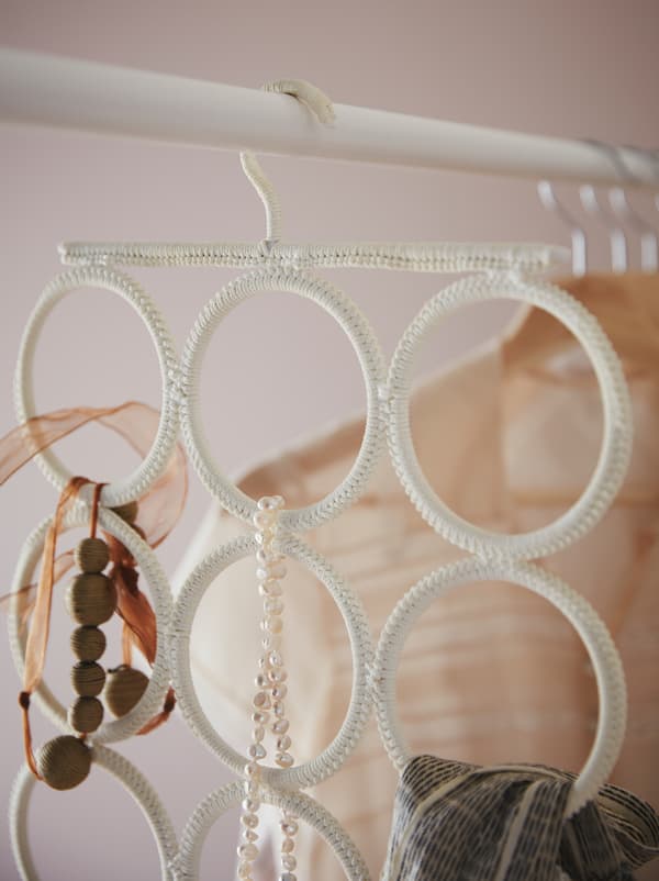 Hanging from a wardrobe rod is a KOMPLEMENT multi-use hanger holding necklaces, a scarf and other accessories.
