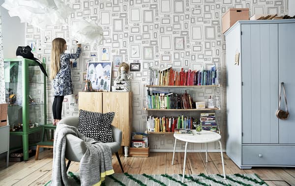 Hania in ihrem Zimmer mit bunten Möbeln, einem grünen Teppich und ihrem Regenbogenbücherregal.