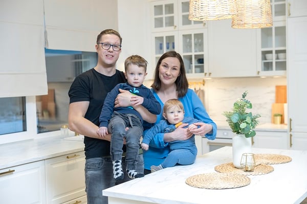 Happy family with two children standing in a bright modern white kitchen.