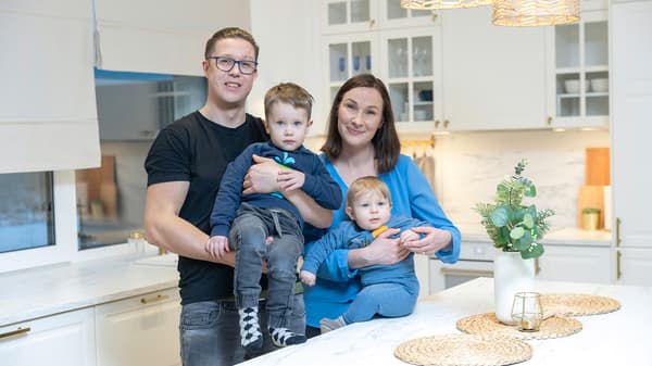 Happy family with two children standing in a bright modern white kitchen.