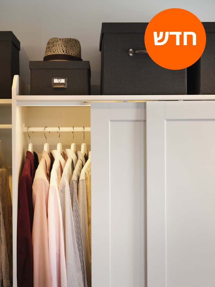 ארון HAUGA משולב עם דלת הזזה פתוחה ובגדים תלויים בפנים. מעל הארון מונחים קופסאות וכובע.