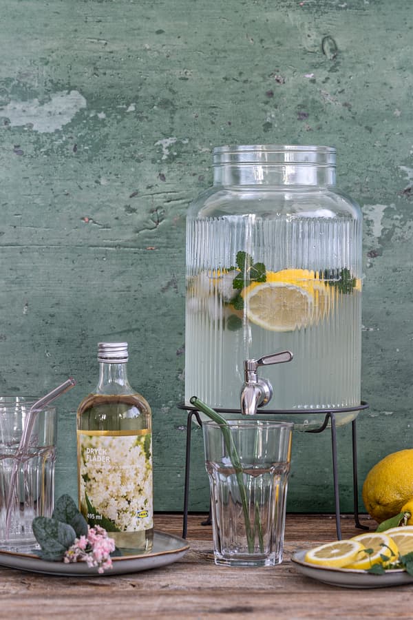 Hausgemachte Holunder-Zitronenlimonade steht in einem Gefäß auf einer Holzplatte.