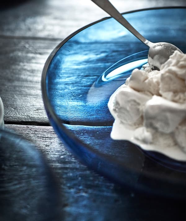 Helado en un plato de cristal azul sobre una mesa de madera oscura.