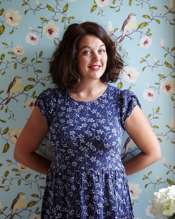 Helena stands against floral wallpaper
