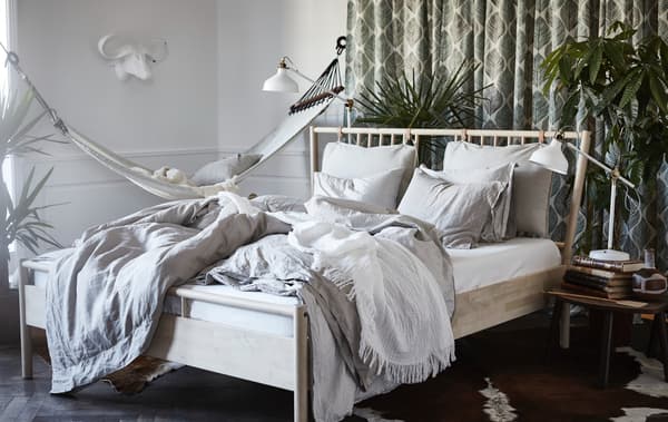 Helles Schlafzimmer mit BJÖRKSNÄS Bettgestell in Birke und einer weißen Hängematte.