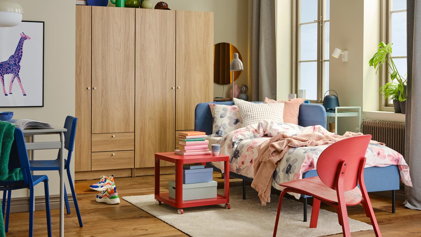 Helles und buntes Studio-Schlafzimmer mit einem BLÅKULLEN Bettgestell mit Eckkopfteil und LAPPNYCKLAR Bettwäsche.