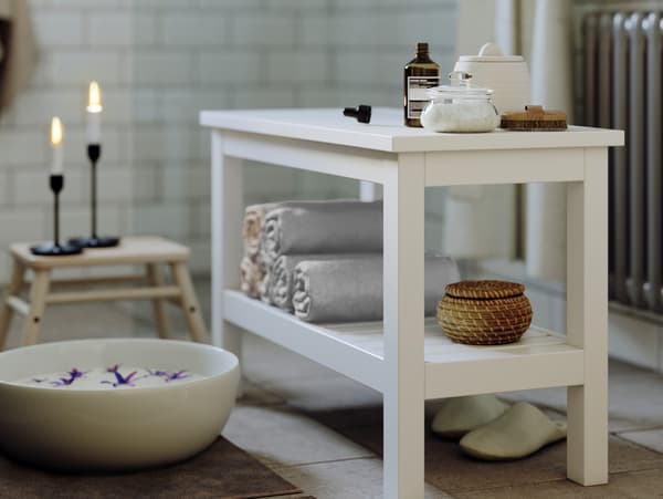 HEMNES bænk står i badeværelse med sterinlys, fodbad og håndklæder ligger på hylden. 