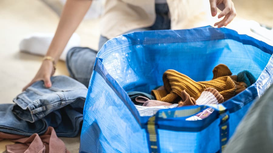 Henkilö pakkaa vaatteita kierrätykseen siniseen IKEA-kassiin.