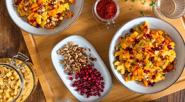 Herbstliche Kürbis-Pasta mit Walnüssen steht frisch angerichtet auf einem Holzbrett.