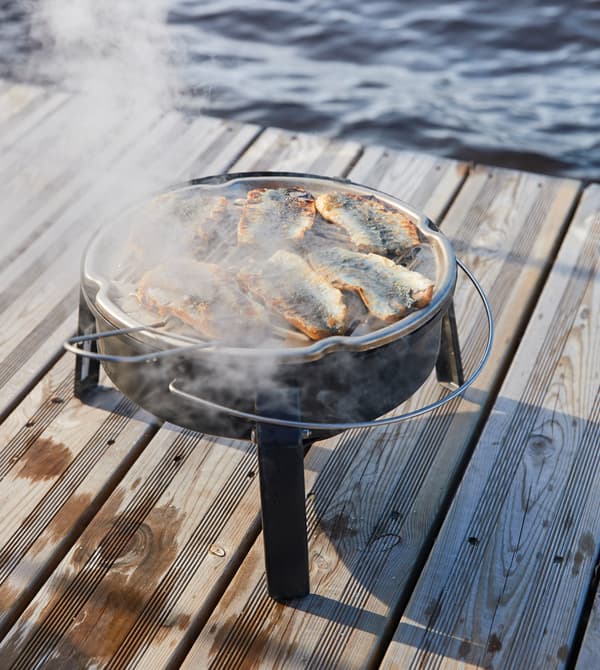 Herring fillets are being grilled on a small charcoal barbeque on a doc.