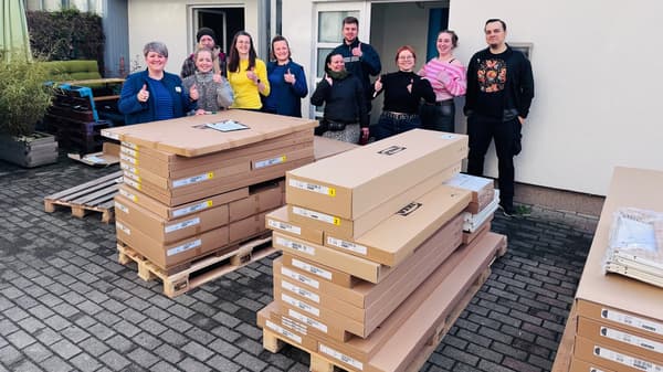 Hier sieht man 10 Personen, die vor 2 Paletten IKEA Ware stehen und einen Daumen nach oben zeigen - Zeigt eine Sachspendenübergabe