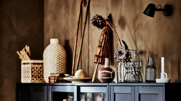 Hjørnet af en stue med et mørkt, bredt HAVSTA skab fyldt med kunsthåndværk af naturmaterialer indvendigt og ovenpå.