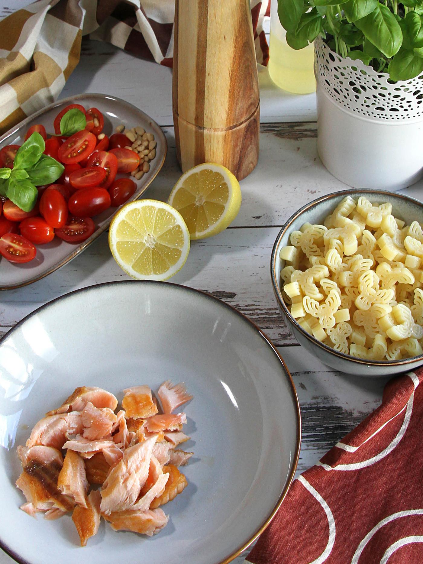 Hlboký tanier GLADELIG s kúskami smaženého lososa, vedľa je miska GLADELIG s cestovinami BÄSTISAR a tanier GLADELIG s nakrájanými cherry paradajkami a bazalkou.