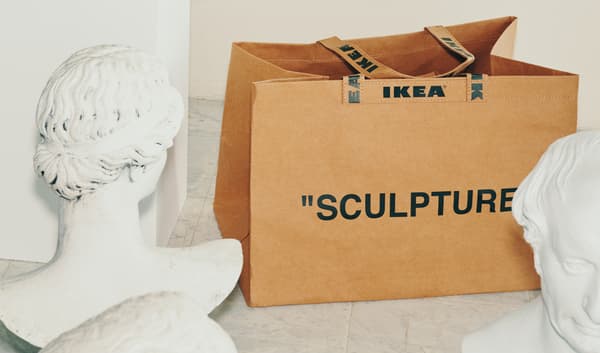 Hnědá taška IKEA s nápisem SCULPTURE, postavená mezi dvěma sochami