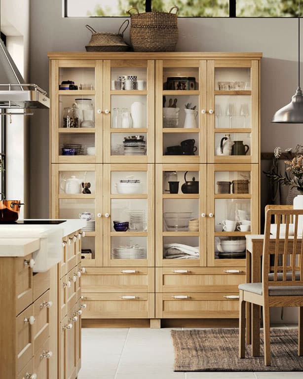 Hölzerne Vitrine mit Geschirr. Davor eine Hölzerne IKEA Küchenlösung mit passendem Essitsch im Landhaus Stil