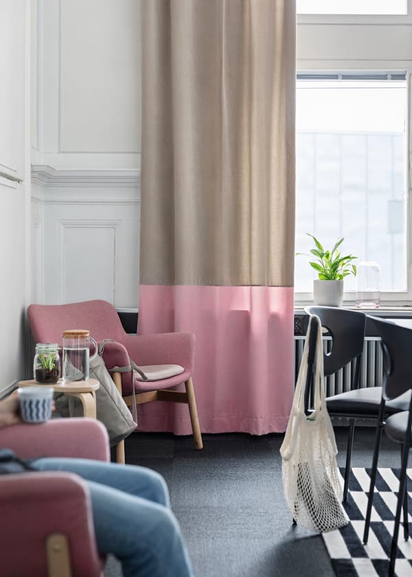 Hörn av konferensrum med två rosa fåtöljer med ett litet bord emellan intill ett stort fönster med beige och rosa gardiner.