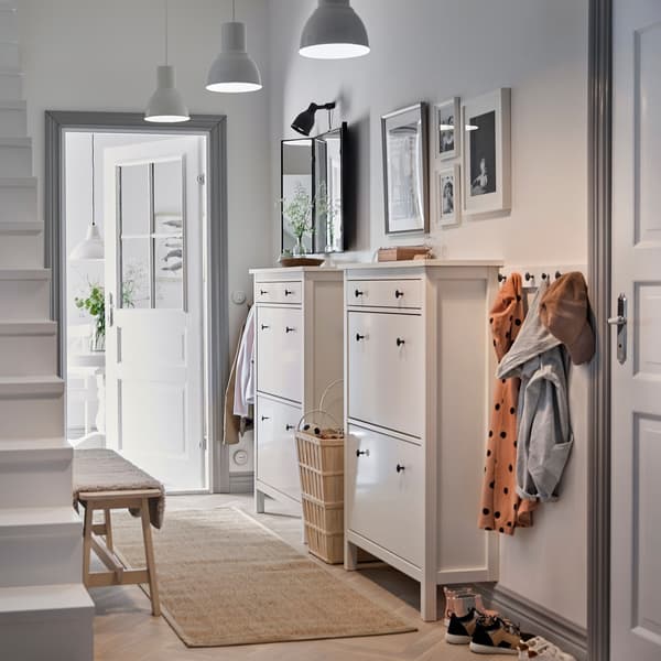 Hol alb cu două dulapuri de pantofi HEMNES albe, în stil tradițional, așezate unul lângă altul, și un șir de cârlige pentru haine.