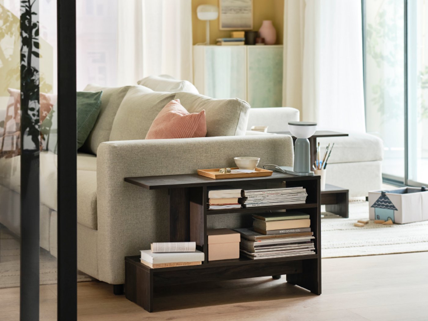 HOLMERUD tafeltje met heel wat boeken op de planken staat naast een VIMLE 3-zitsbank met extra kussens erop.