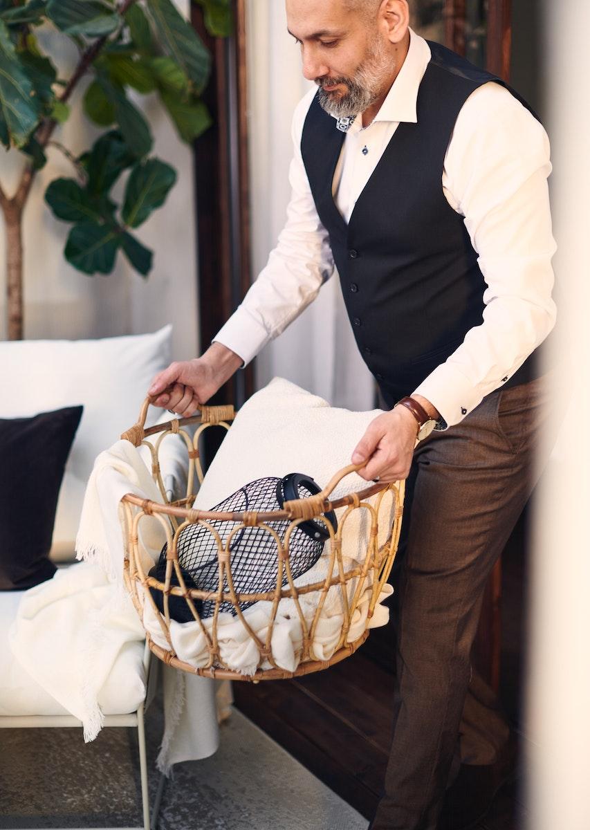 Hombre sosteniendo un canasto organizador de color café con accesorios decorativos en su interior. 