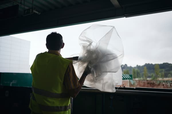 Hombre vestido con chaleco amarillo de construcción botando una bolsa de plástico.