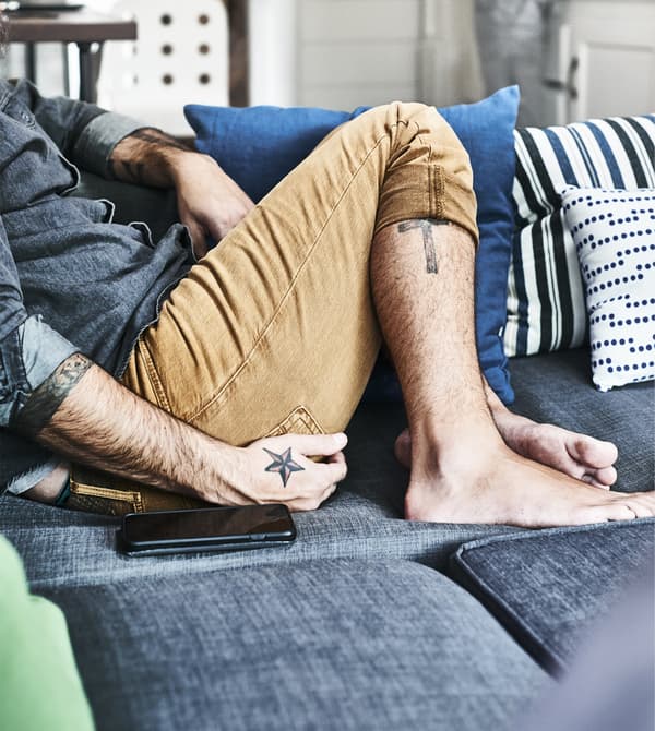Homme assis sur un canapé gris garni d’articles textiles bleus.