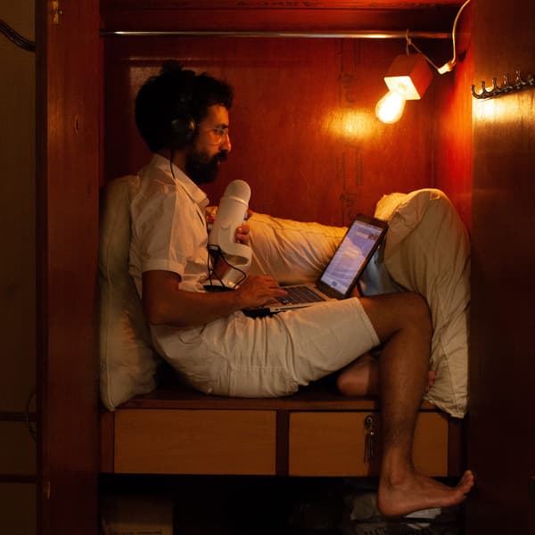 Homme en train d'enregistrer un balado dans son environnement d'enregistrement créé soi-même – son armoire-penderie sert à régler l'acoustique grâce à une couette.