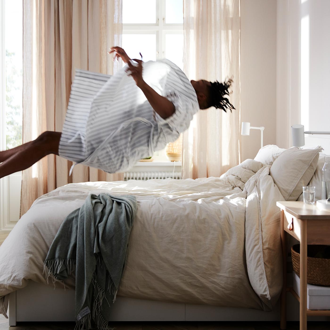 Homme se jetant en arrière sur un lit MALM avec matelas à ressorts ensachés VATNESTRÖM et linge de lit blanc.