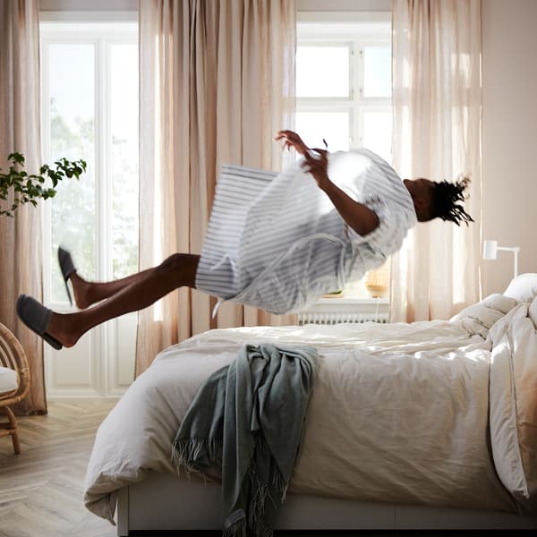 Homme se jetant en arrière sur un lit MALM avec matelas à ressorts ensachés VATNESTRÖM et linge de lit blanc.