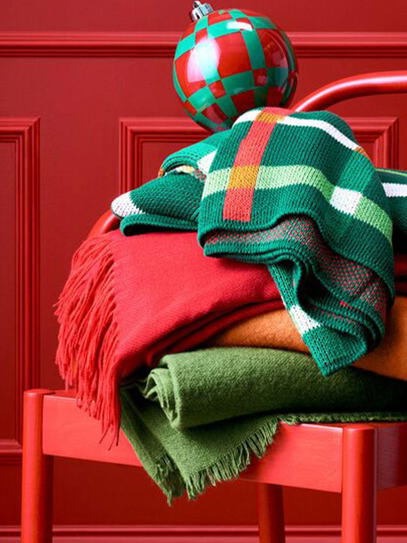 Hopvikta filtar i grönt och rött på en röd stol, med en rutmönstrad julkula ovanpå.