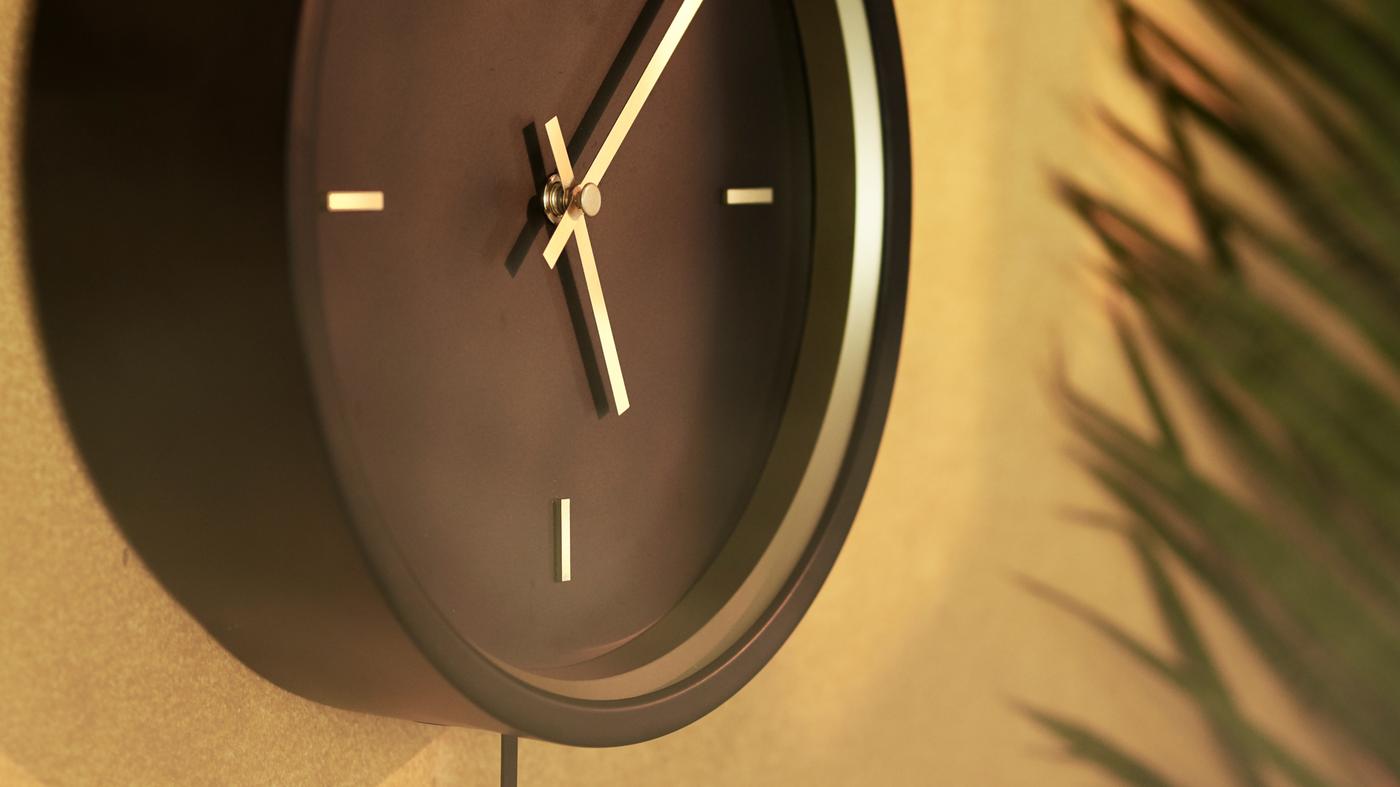 Horma urre-marroi batean zintzilikatutako STURSK hormako erloju beltza, urrezko xehetasun eta orratzekin.