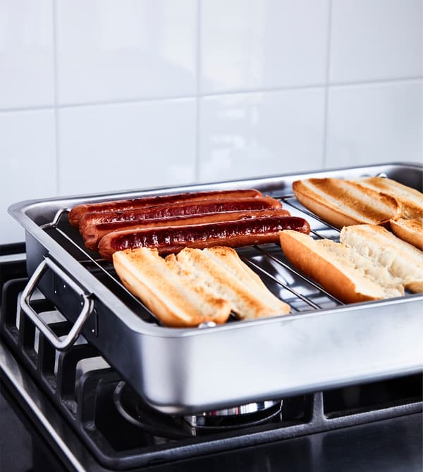 Hotdogs and buns sit on a grillrack on a stove.
