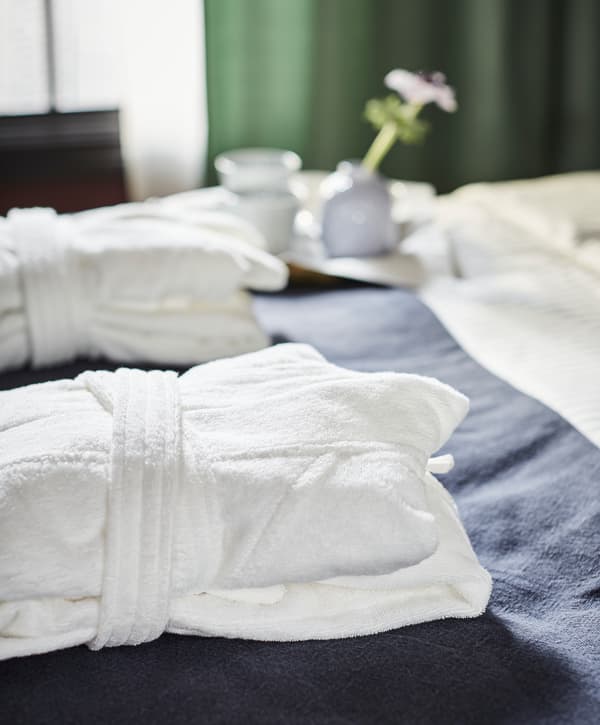 Hotelsko uređenje i dva lepo sklopljena bade mantila na duplom krevetu; poslužavnik sa šoljicama i cvetom.