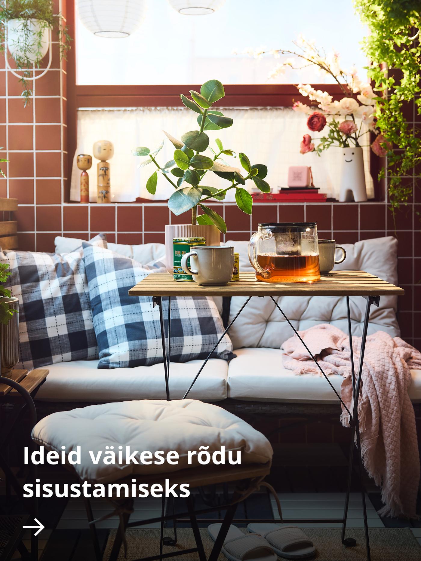 Hubane rõdunurk punastest plaatidest seinaga. Pingil on ruudulised padjad, pingi ees on väike puidust laud kruuside ja klaasist teekannuga. Aknalaual on potitaimed päikesevalguse käes.