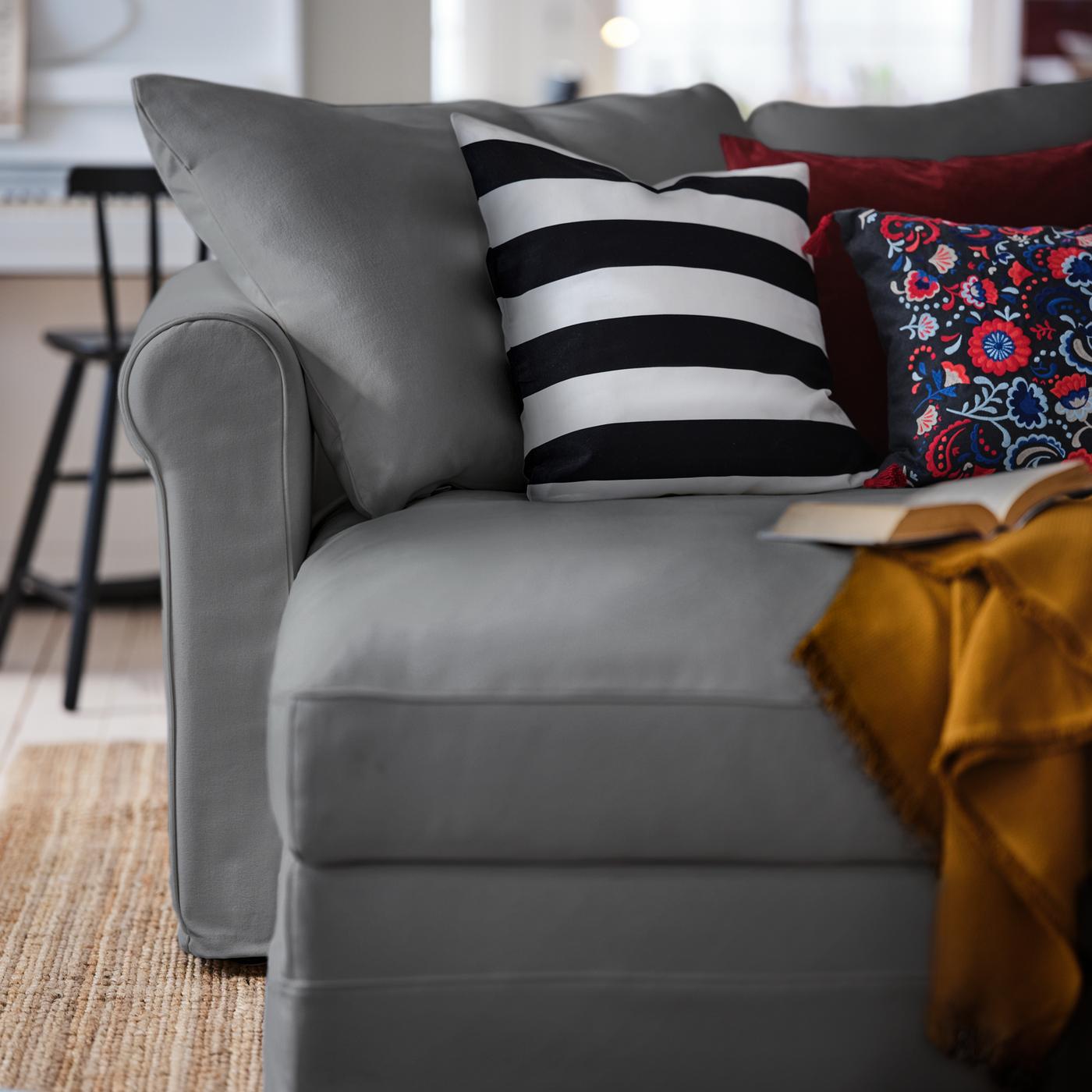 Hujung chaise longue bagi sofa 4 tempat duduk GRÖNLID berwarna kelabu sederhana, dengan pelbagai kusyen berwarna-warni dan tekstil padanya.