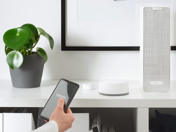 Hvid SYMFONISK wi-fi-højttaler oven på en reol i en stue.