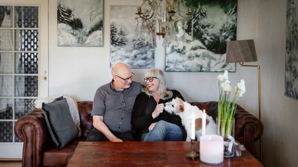 I en soffa sitter en man och en kvinna. Bredvid kvinnan sitter en vit hund. 