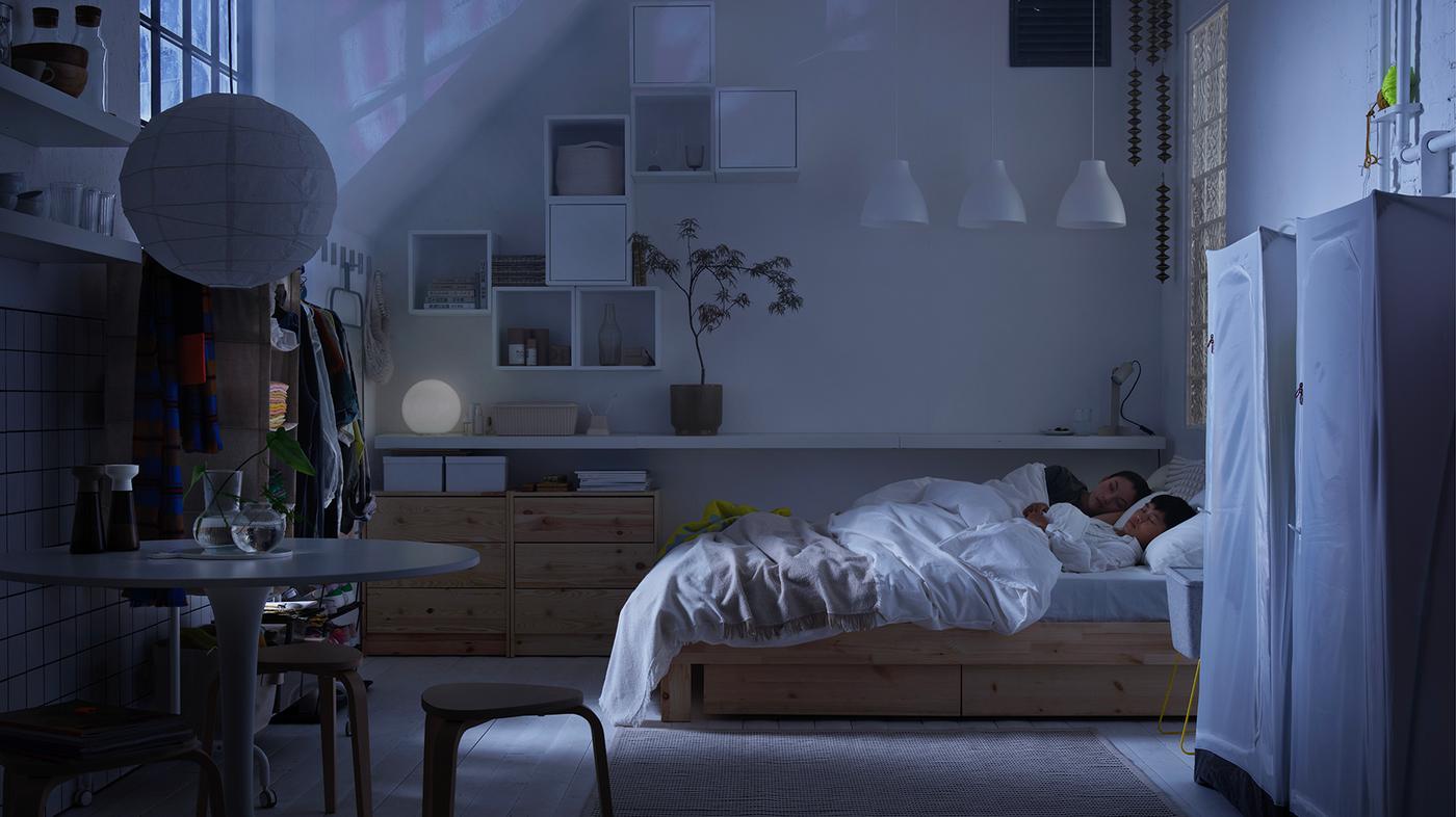 I ett nedsläckt sovrum ligger en förälder och ett barn och sover i en säng.