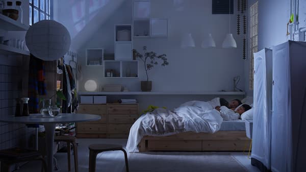 I ett nedsläckt sovrum ligger en förälder och ett barn och sover i en säng.