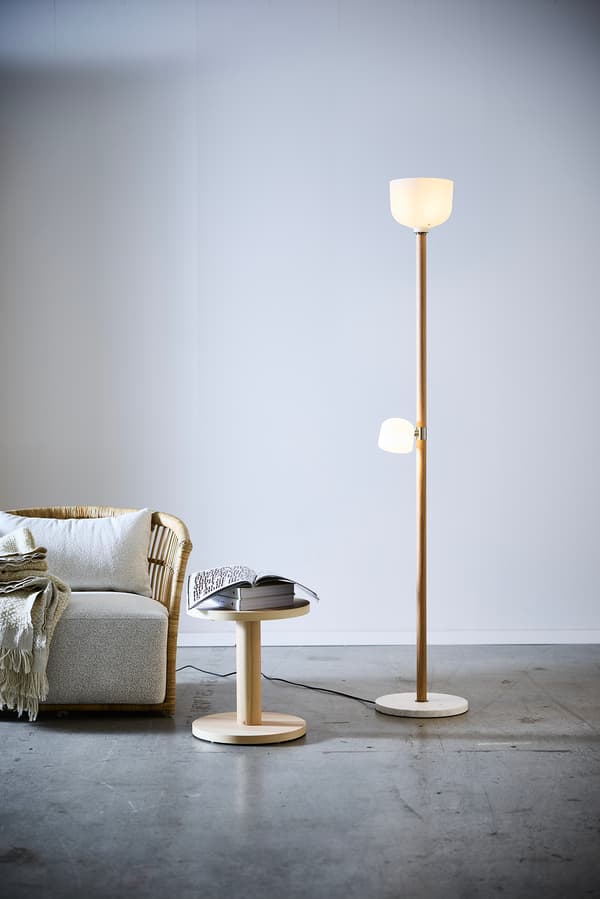 I ett rum med betonggolv står en lampa med ekstång. Bredvid lampan står ett mindre bord och en fåtölj i rotting. 