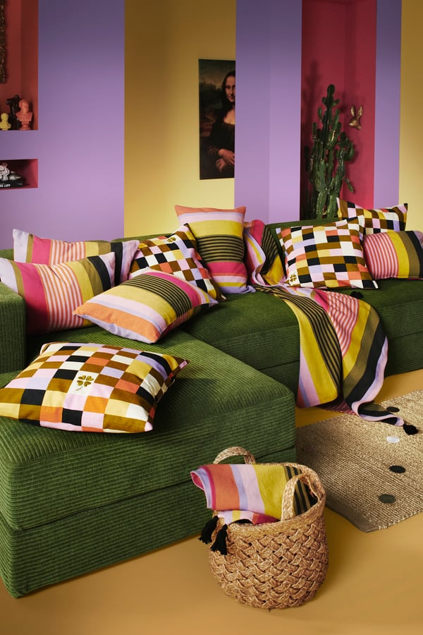 I ett vardagsrum står en grön soffa. På soffan ligger färgglada kuddar. 