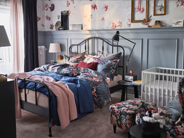 黒いアイアンベッドに花柄寝具を合わせた個性的な寝室。壁の装飾とラグで華やかな雰囲気。