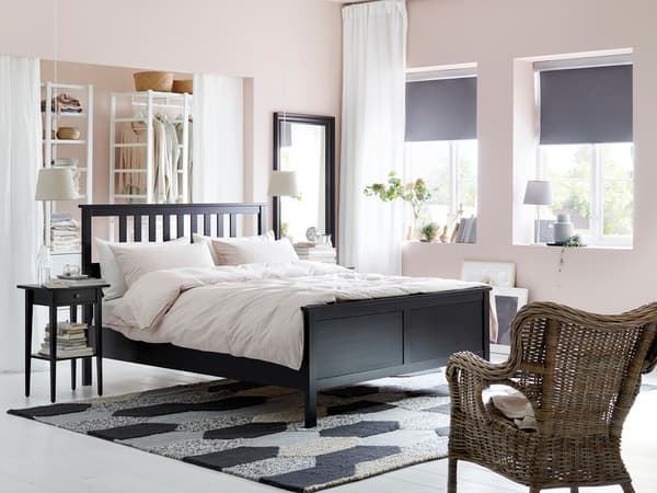 黒いベッドフレームに白い寝具を合わせたシンプル寝室。ラタンチェアとモノトーンラグで北欧風。