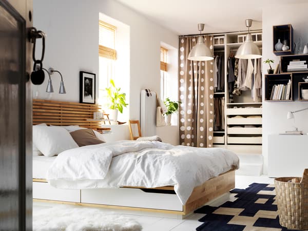 白いベッドと木製ヘッドボードを置いた明るい寝室。ラグとカーテンで北欧風のナチュラルな空間。