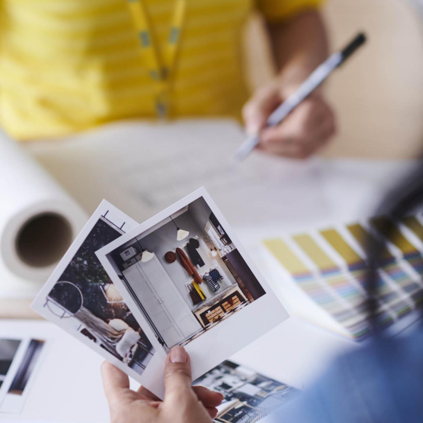 Iemand heeft foto's met inspiratie van zijn huis in zijn hand en zit tegenover een IKEA medewerker.