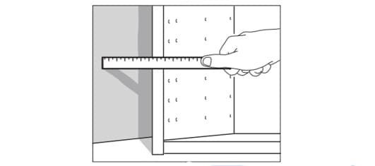 Iemand houdt ee liniaal tegen een keukenkastje om op te meten hoe groot het opvulstuk moet zijn.