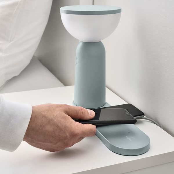 Iemand legt zijn telefoon op de mob led-lamp om draadloos opladen, dimbaar licht grijsblauw